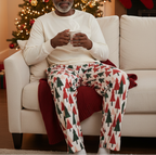 Unique older Black man wearing Christmas Tree men’s pajama pants with an ivory shirt in a holiday lounge