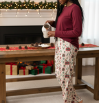 Black woman wearing the Christmas Present women’s pajama pants while pouring hot cocoa in a festive dining room