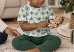 Toddler wearing Green Snowflake kids pajama top while holding a wooden snowflake ornament indoors