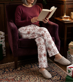 Woman reading in a library wearing Red Snowflake pajama pants and a burgundy lounge top