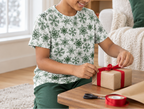 Child wearing green snowflake kids pajama top while wrapping a gift