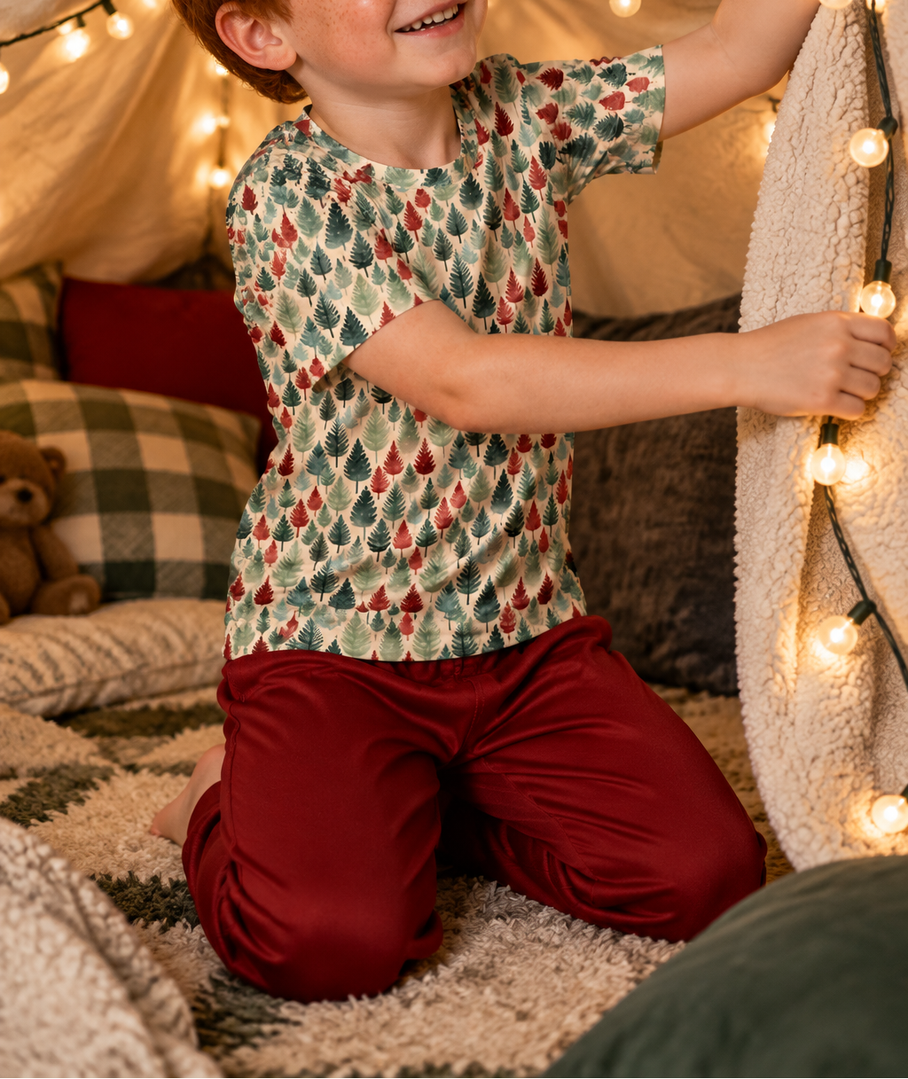 Boy in Leafy Dreams pajama top building a blanket fort with string lights