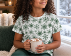 Child wearing green snowflake kids pajama top enjoying cocoa by a winter window