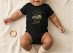 Baby wearing a black Garden Fresh onesie beside a wooden teething ring, with the chest design visible.