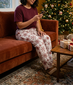 Woman listening to an audiobook wearing Red Snowflake pajama pants and a burgundy lounge top