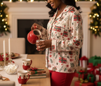 Black woman wearing the Christmas Present women’s long sleeve pajama top while pouring hot cocoa in a festive dining room