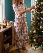 Woman decorating a Christmas tree wearing Red Snowflake pajama pants and matching white-trim shirt
