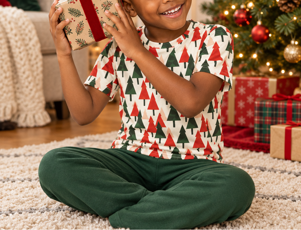 Child in Christmas Tree kids pajama top shaking a present by the tree