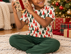 Child in Christmas Tree kids pajama top shaking a present by the tree