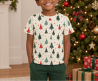 Child wearing a cream Christmas tree pajama top beside a decorated holiday tree