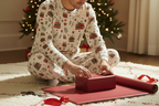 East Asian man wearing Christmas Present pajamas while wrapping a holiday gift