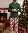 Unique South Asian man wearing Christmas Tree men’s pajama pants with a forest green shirt beside a Christmas tree
