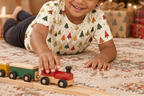 Child wearing Spring Christmas kids pajama top while playing with a toy train under the tree