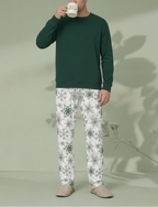 Man sipping from a Merry Christmas mug in Green Snowflake pajama pants