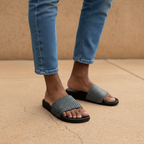 Person wearing black and gray patterned sandals with rolled-up blue jeans on a beige background