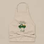A beige fabric apron with a neck loop and waist tie, featuring a green graphic of a vintage pickup truck carrying a garden hose, with the words 'GARDEN Fresh' printed on the front.