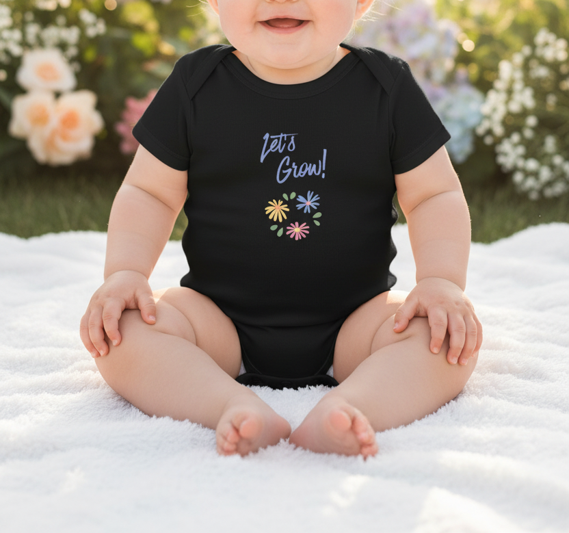 A baby sitting outdoors on a white blanket wearing a black short-sleeve bodysuit with the text 'Let's Grow!' and small colorful flower graphics on the front.