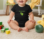 A baby sitting on a cream carpet in a playroom, wearing a black short-sleeve bodysuit with a green leaf graphic and the text 'BABY BAY LEAF'.