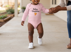 Pink Carrot onesie on a toddler in sneakers walking beside mother