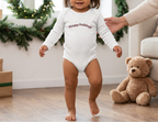 Toddler girl with longer dark hair walking in the White Happy Holidays onesie