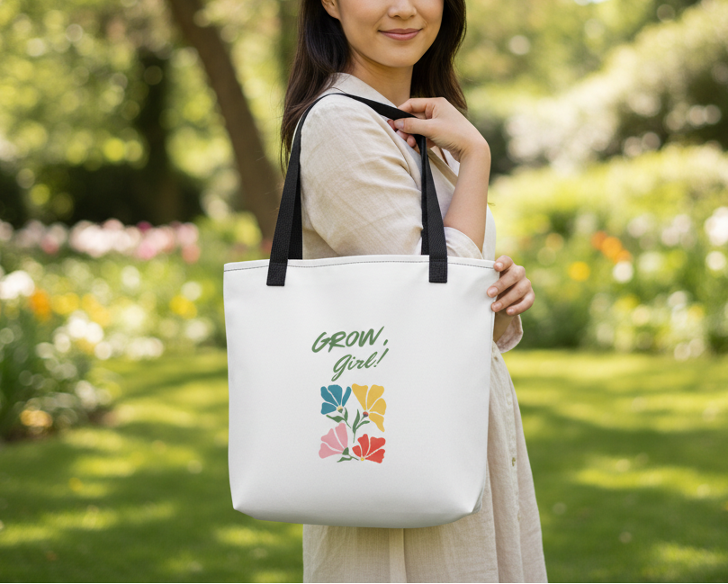 Woman holding a white tote bag with 'Grow Girl!' and flower designs in a garden setting