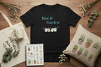 A black short-sleeve graphic T-shirt laid flat on a wooden surface, surrounded by styled props including a cream tote bag, a mug, a small notebook with gardening illustrations, a pillow with potted plants, and dried flowers. The shirt reads 'Rise & Garden' in teal above a small clothesline graphic with colorful tags.