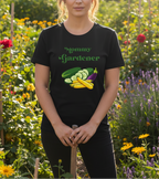 A woman wearing a black graphic t-shirt that reads 'Mommy Gardener' with illustrations of zucchini and eggplant, standing in a sunny garden holding a garden tool.